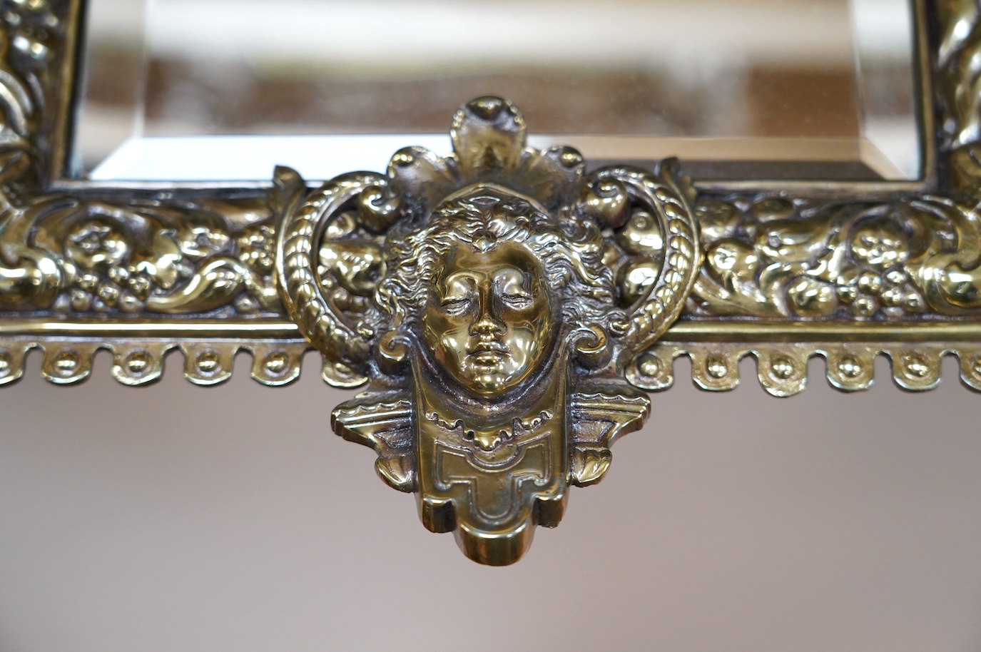 A pair of French brass repoussé mirrors with an ornate putti top and mask decorated bottom, 49cm high. Condition - good